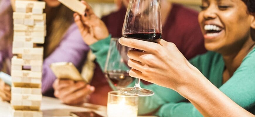 Four friends gathered around a living room table playing jenga and drinking from wine glasses