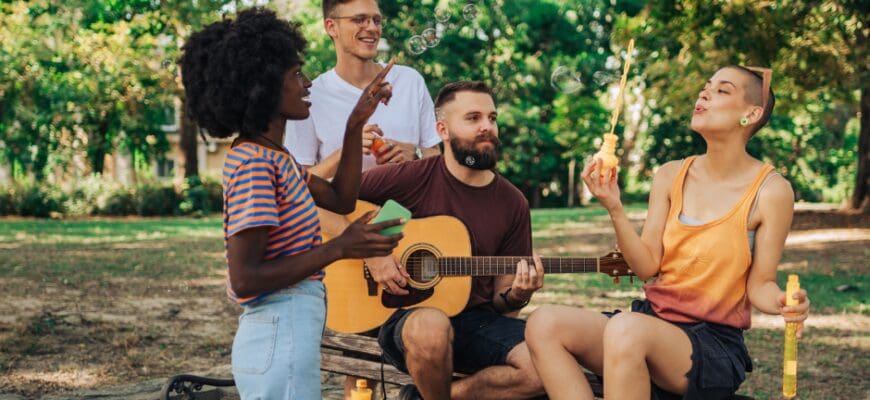 Four friends gathered around a park bench, one playing a guitar