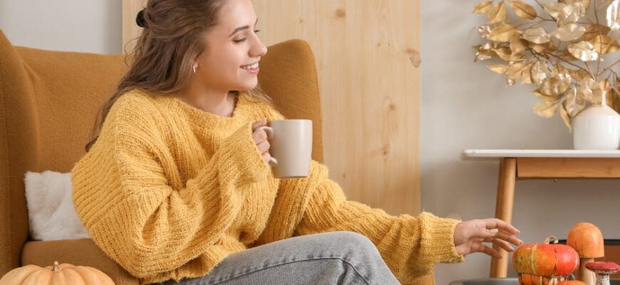 A woman sitting in a chair holding a mug, with fall decorations around her